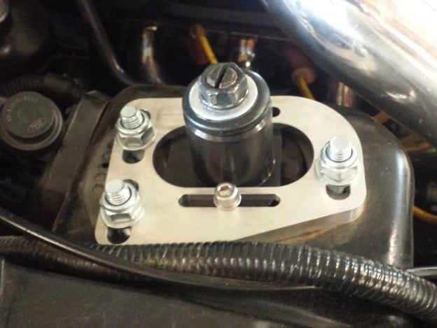 Adjustable caster/camber plate installed on a vehicle's front strut tower, allowing suspension alignment changes to fine-tune camber and caster angles.
