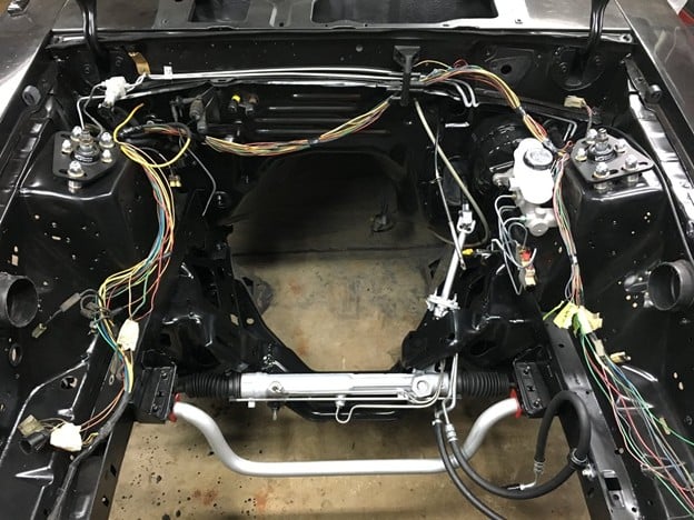 Engine bay with the engine removed, showing adjustable caster/camber plates installed on the front strut towers as part of a suspension and steering rebuild.