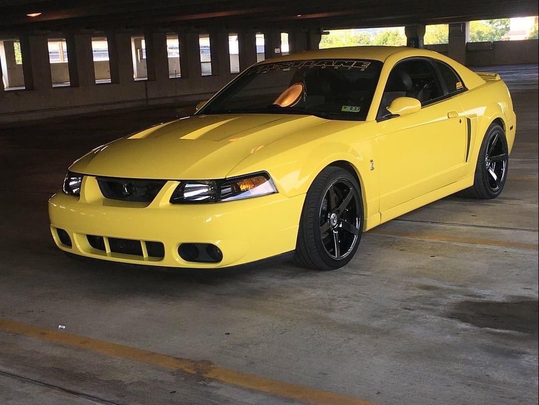 Yellow 2003–2004 Ford Mustang SVT Cobra Terminator with black aftermarket wheels parked in a parking garage.