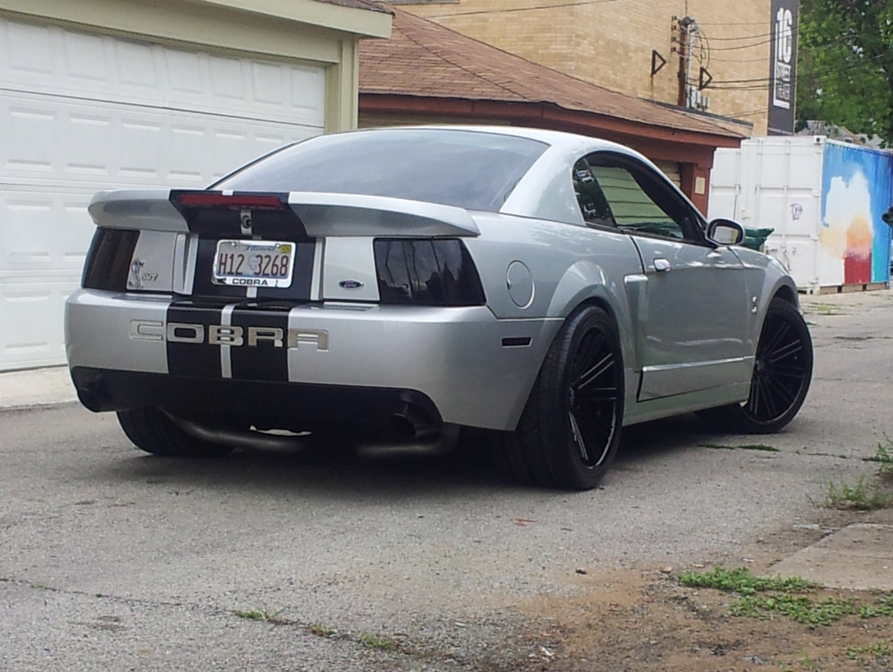 Silver 2003–2004 Ford Mustang SVT Cobra Terminator with black wheels, smoked taillights, and Cobra rear bumper graphics parked in an alley.